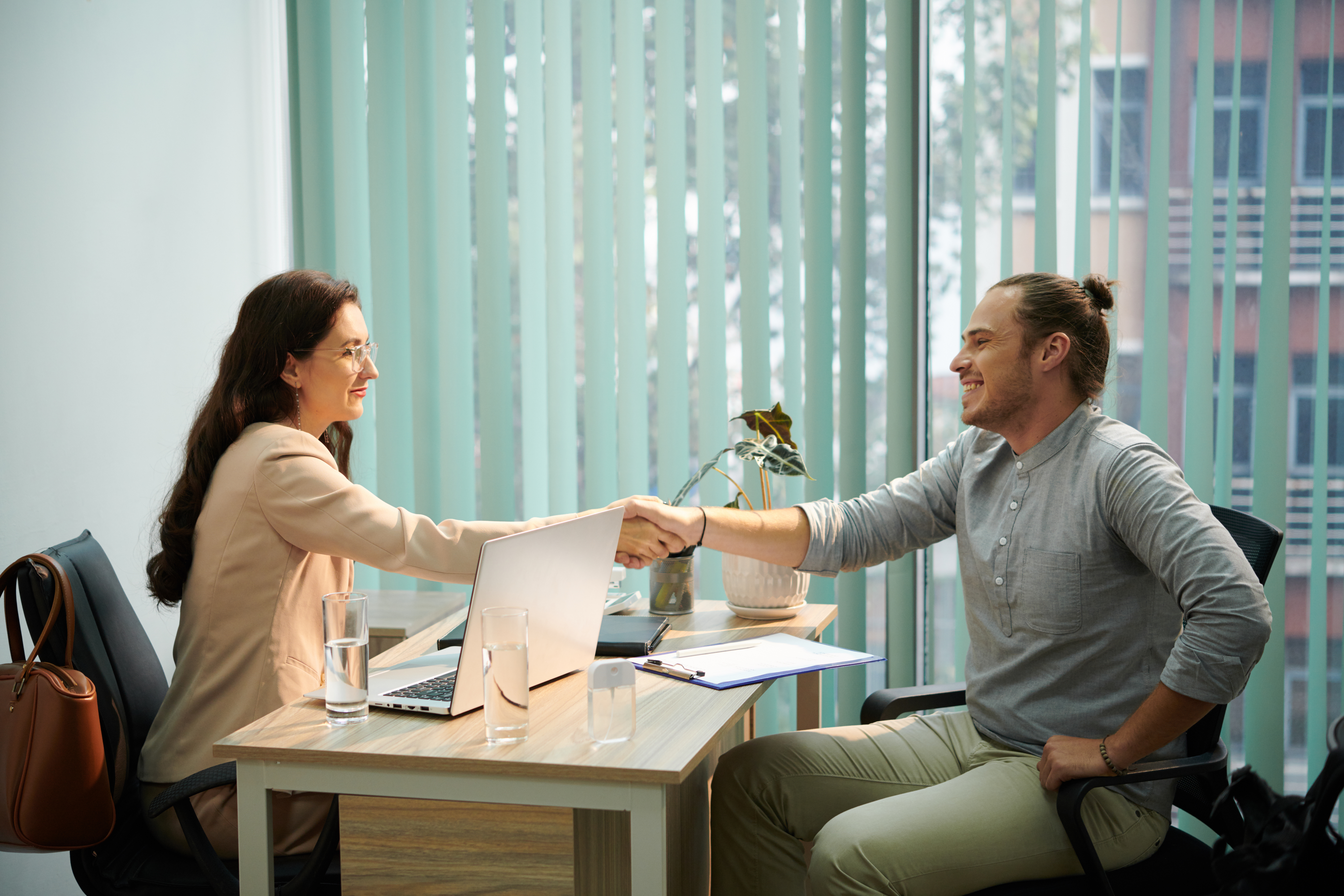 male and female coworkers shaking hands over a desk